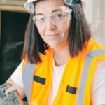Female construction worker wearing PPE, holding a wrench in an indoor setting.